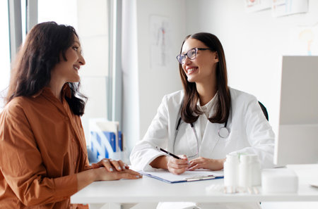 Friendly woman doctor therapist and female patient sitting and talking, looking at each other in medical clinic office during consultationの写真素材