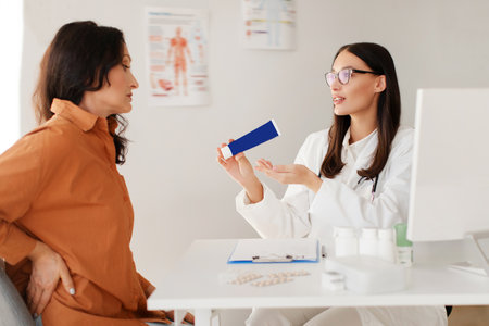 Doctor recommending medicine to female patient suffering with pain in lower back of vertebral discs. Female general practitioner holding tube of ointmentの写真素材