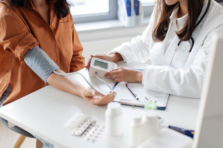 Young lady examining female patient measuring arterial blood pressure with tonometer medical device, sitting at table. Hypertension health problem conceptの写真素材
