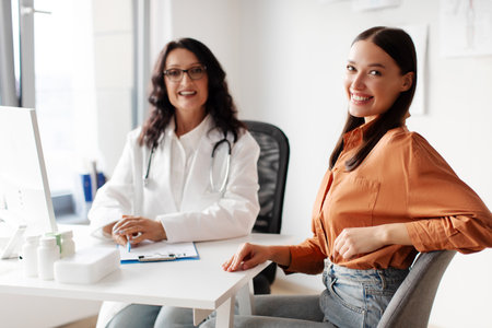 Portrait of happy lady patient sitting at doctors office, enjoying quality medical services in clinic, female therapist in uniform sitting at deskの写真素材