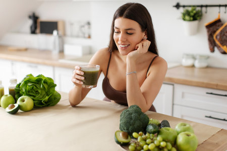 Slim happy lady drinking detox smoothie, enjoying healthy drink in kitchen modern interior. Nutrition for weight lossの写真素材