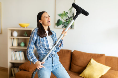 Joyful lady finding joy in chores, using vacuum cleaner in her stylish living room, free spaceの写真素材