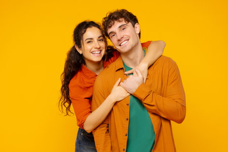 Romantic relationship. Smiling European couple enjoying time together, woman embracing man from back, standing over orange backgroundの写真素材