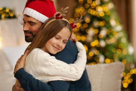 Loving teen daughter embracing her father while spending Christmas together at home, girl wearing deer horns, man in Santa hat, free spaceの写真素材