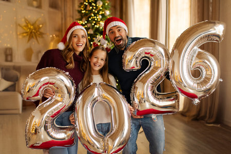 Overjoyed family celebrating Christmas at home, having fun holding giant balloons shaped as numbers 2026の写真素材