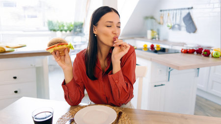 Happy satisfied woman eating pizza with pleasure and enjoying tasty meal, sitting at kitchen table, free spaceの写真素材