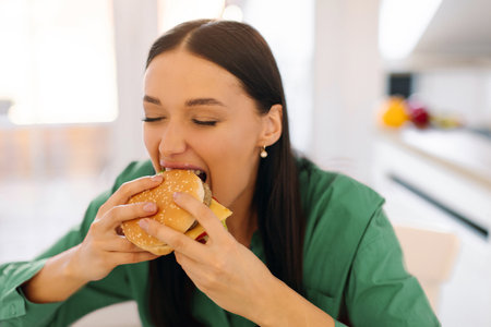 Fast food concept. Happy lady eating tasty burger, holding junk food with meat and biting, enjoying cheat meal for lunch. Unhealthy snackの写真素材