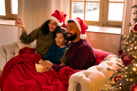 Joyful family relaxing on couch, enjoying popcorn and movie at Christmas Eve, creating joyful holiday atmosphere in decorated living roomの写真素材