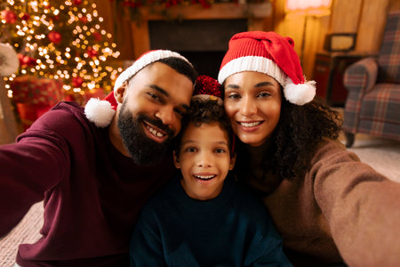 Happy Latin family taking selfie at Christmas Eve, wearing Santa hats, sitting in warm festive decorated living roomの写真素材