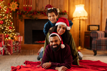 Cheerful African American family posing together in warm living room decorated for winter holidays, lying on carpet in front of Christmas treeの写真素材