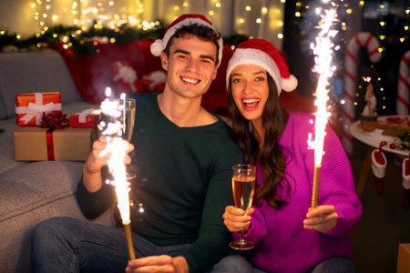 Joyful spouses holding sparkles and champagne glasses, celebrating New Year together at home and smiling at cameraの写真素材