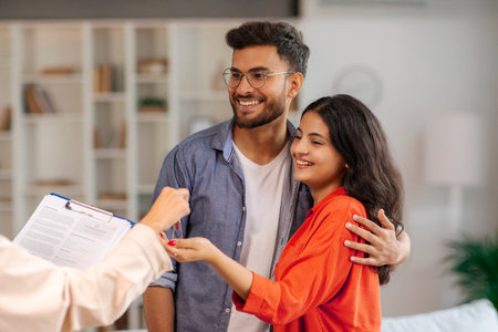 Real estate agent giving keys to young indian buyers, happy woman taking key of future new apartment, spouses buying new houseの写真素材