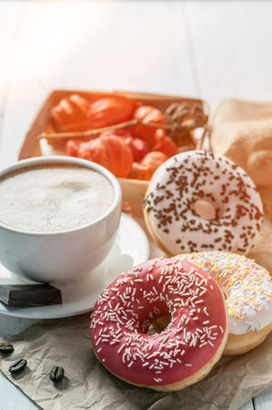 Three donut and a cup of coffee with chocolate on a white tableの写真素材