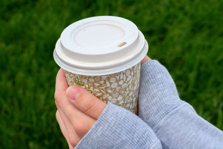 Female hand with paper cup of coffee outdoors, closeup
