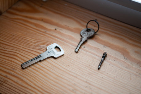 A close-up view of two old, worn metal keys and a single small screw resting on a light-colored wooden surface. The scene is captured with a shallow depth of field.