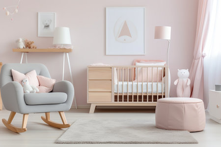 A modern nursery with a pink and gray color scheme. The room features a crib, armchair, ottoman, and two lamps. The walls are decorated with framed art.の素材