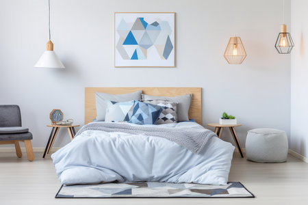 a modern bedroom with a wooden bed, white walls, and a geometric blue and white rug. The room has a minimalist design with a wooden nightstand, a gray armchair, and a white pouf. The bed is made with white and blue bedding and has a wooden headboardの素材