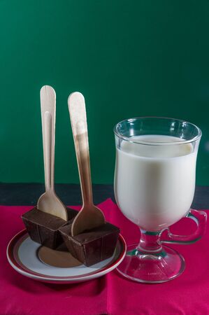 Belgian hot chocolate stirrers with milk in glass mug, purple napkin green background.の写真素材