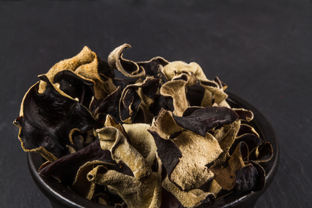 Black ceramic bowl with dried mushrooms piled in, Auricularia polytricha, Cloud ear Mushroom or Chinese Black Mushroom. Close up blue slate background.の写真素材