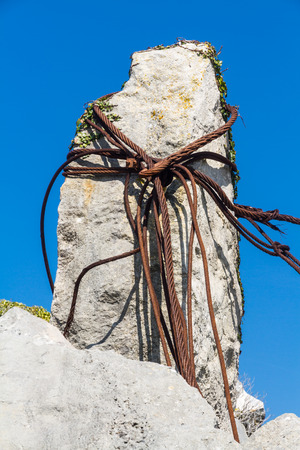 Old rusty iron cables looped around a limestone rock in a quarry.の写真素材