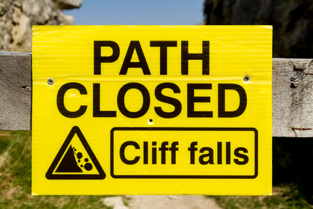 Yellow sign warning that path closed due to cliff falls.の写真素材