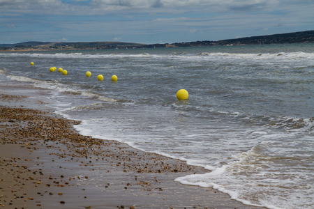 UK pebble beach with line of yellow buoys.の写真素材
