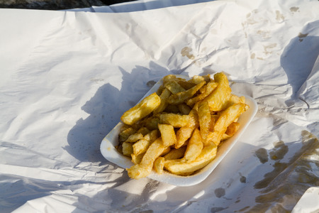 Portion of British chips or fries, in carton with wrapping paper on a sunny day.の写真素材