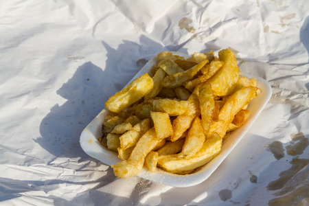 Portion of British chips or fries, in carton with wrapping paper on a sunny day.の写真素材