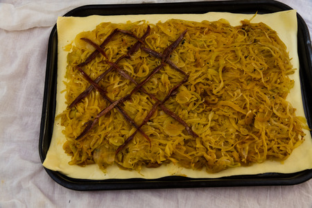 Adding anchovy lattice on to the cooked onions on puff pastry when making pissaladiereの写真素材