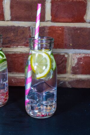 Childrens healthy water with ice, lemon, lime, pomegranate seeds and straws.の写真素材