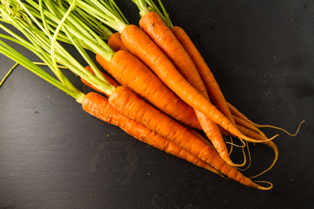 Carrots or Daucus carota bunch with leaves on a dark slate background.の写真素材