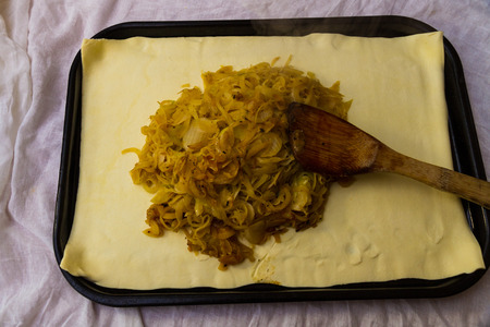 Spoon cooked onions on to puff pastry when making pissaladiereの写真素材