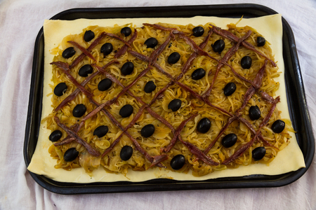 Anchovy lattice and olives on cooked onions on puff pastry when making pissaladiere, ready for cooking.の写真素材