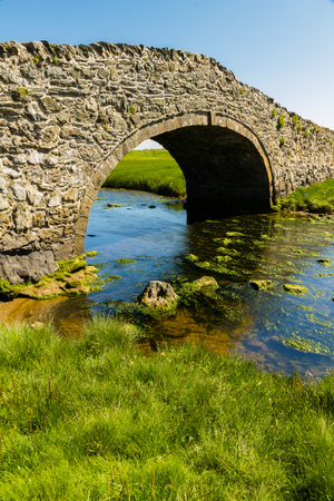 Eighteenth Century stone hump back bridge, with water channel, the river Ffraw, and blue sky....