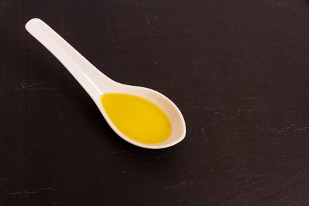 Olive oil presented in a ceramic spoon with a slate background, macro.の写真素材