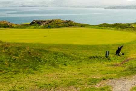 Clifftop putting green with bag and sea, Nefyn & District Golf Club, Morfa Nefyn, Llyn Peninsula, Gwynedd, Wales, United Kingdomの写真素材