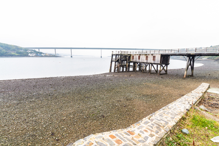 Old wooden jetty with the Cleddau Bridge in the background. Burton Ferry, Pembrokeshire, Wales, United Kingdom.の写真素材