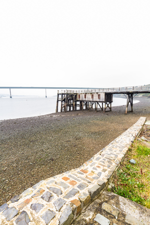 Old wooden jetty with the Cleddau Bridge in the background. Burton Ferry, Pembrokeshire, Wales, United Kingdom.の写真素材
