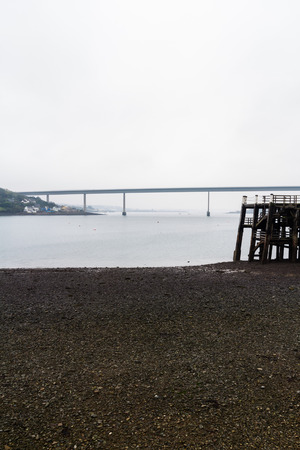 Old wooden jetty with the Cleddau Bridge in the background. Burton Ferry, Pembrokeshire, Wales, United Kingdom.の写真素材