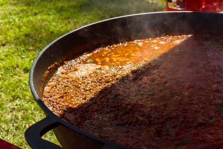 Part shade and sunshine, chilli con carne cooking in a commercial paella pan.の写真素材