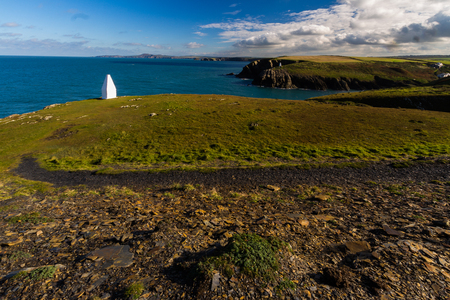 The west welsh coast, with white obelisk forming maker to entrance to harbour. Porthgain, Pembrokeshire, Wales, United Kingdom.の写真素材