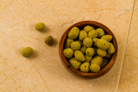 Small wooden bowl filled with wasabi covered peanuts.の写真素材