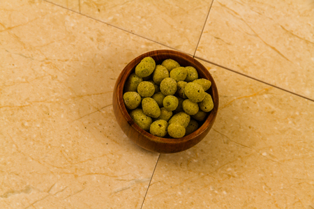 Small wooden bowl filled with wasabi covered peanuts.の写真素材