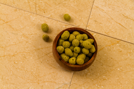 Small wooden bowl filled with wasabi covered peanuts.の写真素材