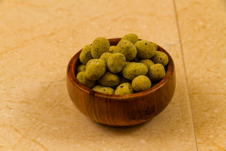 Small wooden bowl filled with wasabi covered peanuts.の写真素材