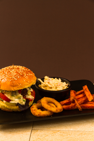 Gourmet beef burger, with salad, blue cheese sauce, sweet potato fries, onion rings and coleslawの写真素材