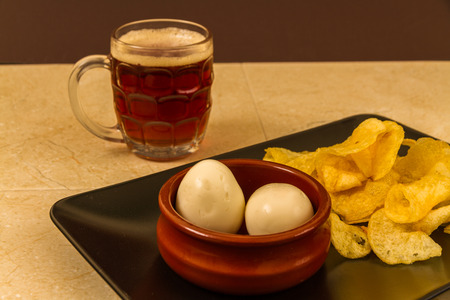 Two pickled eggs in ceramic bowl, served with crisps or chips and half pint of English beer.の写真素材