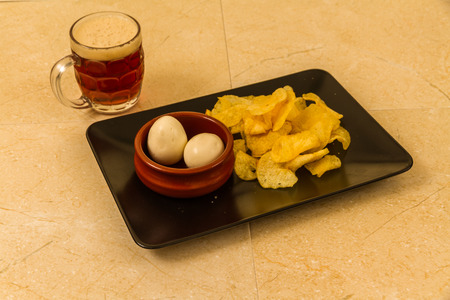 Two pickled eggs in ceramic bowl, served with crisps or chips and half pint of English beer.の写真素材