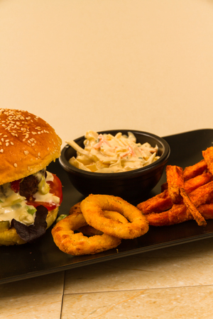 Gourmet beef burger, with salad, blue cheese sauce, sweet potato fries, onion rings and coleslawの写真素材
