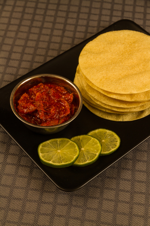 Indian poppadums stacked with bowl of lime pickle and sliced limeの写真素材